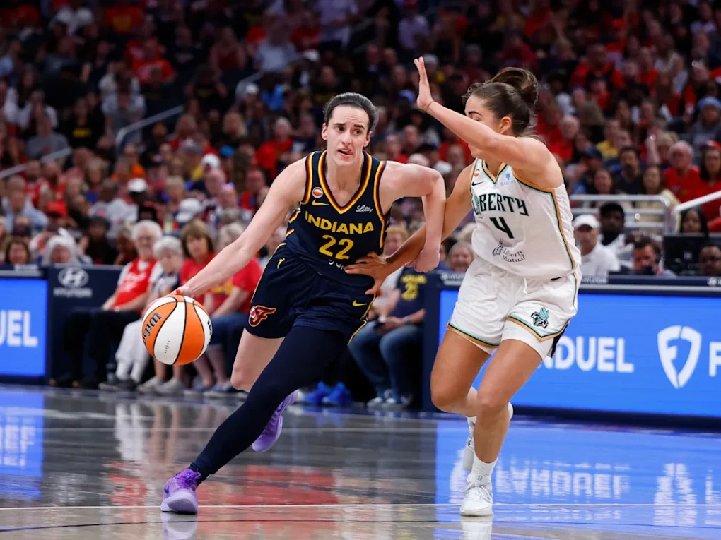 Caitlin Clark driving past New York Liberty defenders during an intense Indiana Fever WNBA game